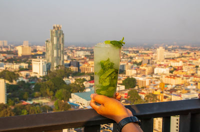 Person holding drink against buildings in city