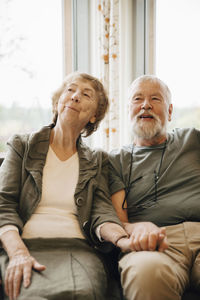 Senior couple holding hands while sitting against window at nursing home