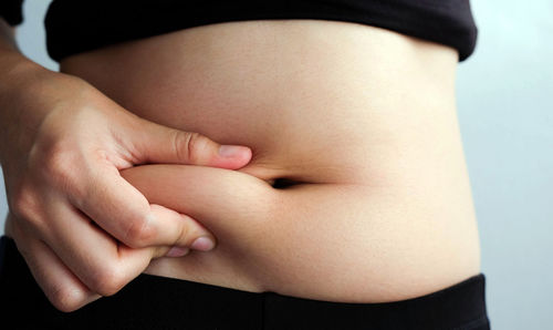 Midsection of woman touching stomach against white background