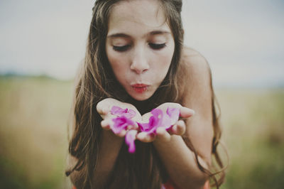 Cute girl blowing pink flower petals on field
