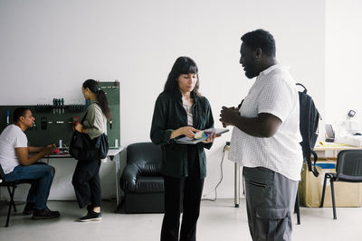 Side view of young male customer discussing with female technician holding laptop at repair shop