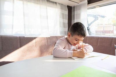 6-year-old caucasian boy paints inside caravan on weekend trip.