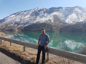 Portrait of smiling man standing against lake and snowcapped mountains