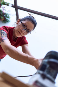 Young woman polishing a wooden plank with a power sander