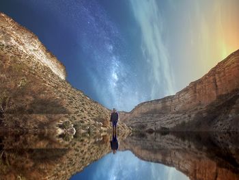 Reflection of woman and rock formation in lake against sky at night