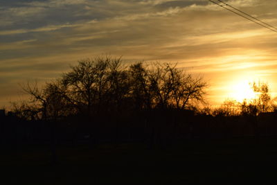 Silhouette trees on landscape against sky at sunset