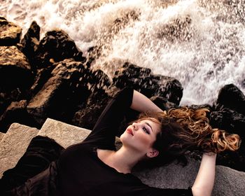 High angle view of thoughtful young woman lying by sea