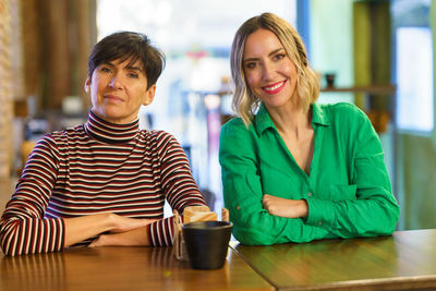 Portrait of smiling woman using mobile phone while sitting on table