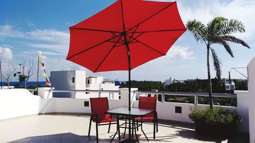 Chairs and table under red parasol at restaurant against sky