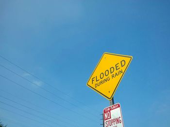 Low angle view of a flooded during rain road sign and a no stopping sign against clear blue sky.