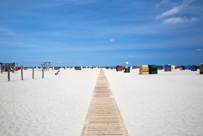 Hooded beach chairs on sand against blue sky during sunny day