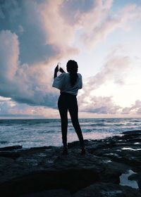 Full length rear view of woman photographing while standing on beach