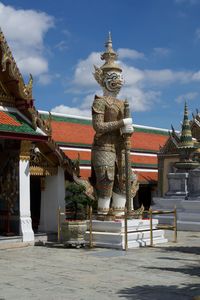 Statue of demon guardian in front of historic temple building against sky