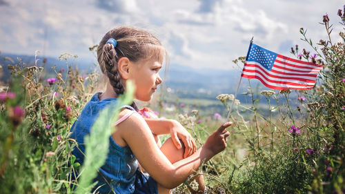 Patriot and national flag day celebration. little patriot sitting on the meadow and holding usa flag