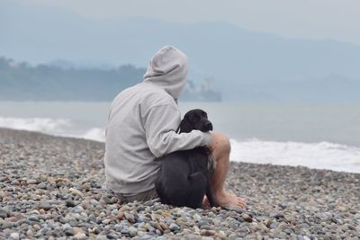 Full length of man sitting on pebbles at beach
