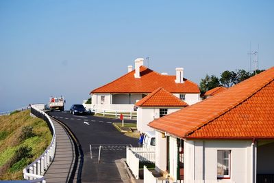 Road by houses against clear blue sky