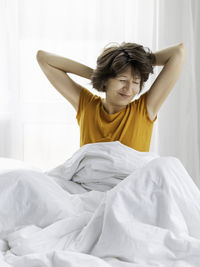 Sleepy woman in yellow pajama is stretching in bed. waking up early in morning. 