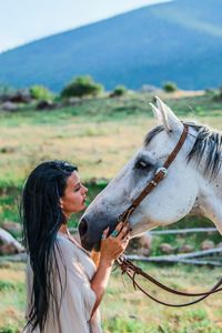 Side view of young woman with horse on field