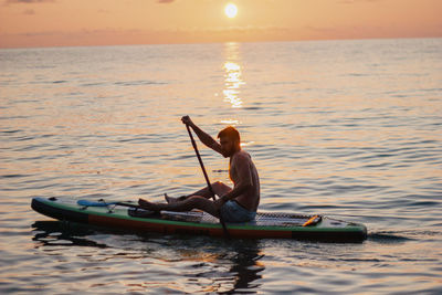 Silhouette man in boat in sea during sunset