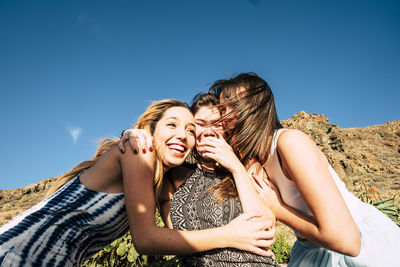 Happy friends sitting against blue sky