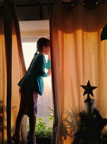 Side view of girl standing by window at home