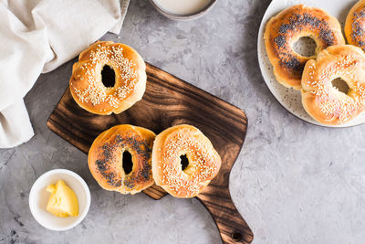 Bagels with poppy seeds and sesame on the board and butter in a bowl on the table.