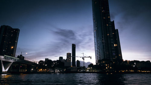 River by illuminated buildings against sky at dusk