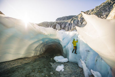 Rear view of man ice climbing outside of glacial cave.