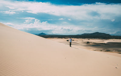 Man standing on sand dune at desert against cloudy sky