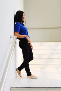 Side view of woman looking away while sitting on floor against building