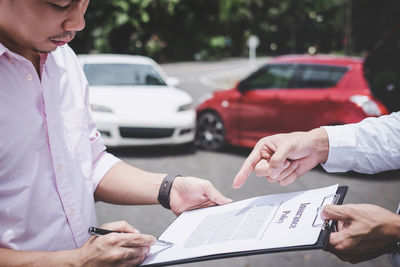 Midsection of businessman pointing at contract to man standing on road