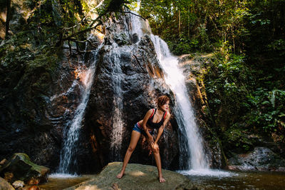 Mid adult woman bending on rock against waterfall