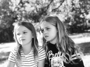 Close-up of sisters looking away against trees