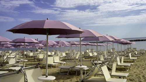 Deck chairs and tables on beach against sky
