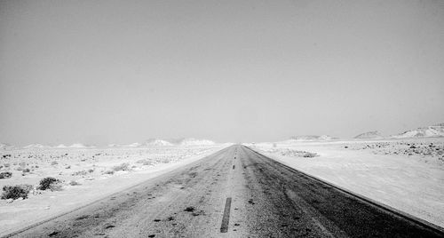 Road amidst snowcapped landscape against clear sky