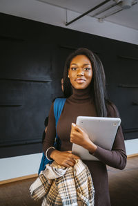 Portrait of smiling young woman holding laptop at community college