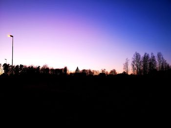 Silhouette trees on field against clear sky during sunset