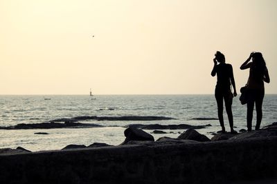 Silhouette people on beach against sky during sunset