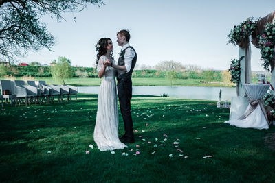 Friends standing on grassy field against clear sky