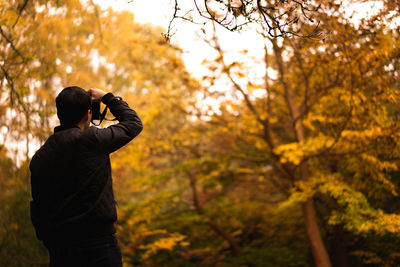 Rear view of photographer photographing autumn trees in park