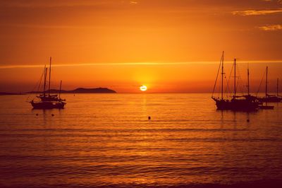 Silhouette boat sailing on sea against orange sky