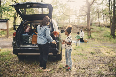 Full length of woman and daughter unloading luggage from electric car trunk at park