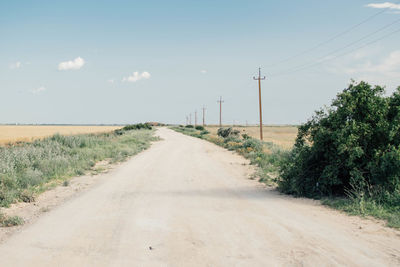 Dirt road amidst field against sky