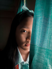 Close-up portrait of young woman by curtain