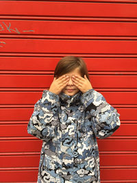 Girl covering eyes while standing against red wall