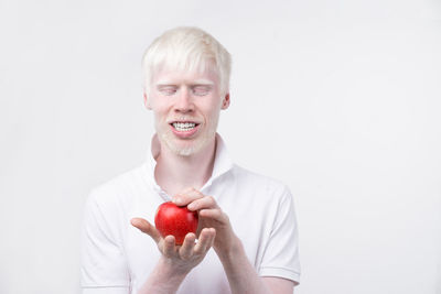 Portrait of smiling man holding apple against white background