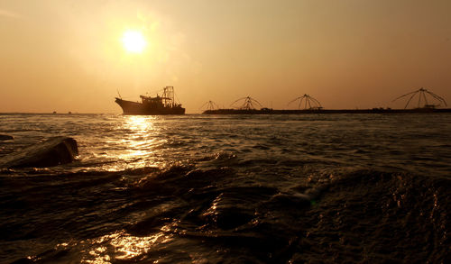 Silhouette boat on sea by fishing nets against orange sky