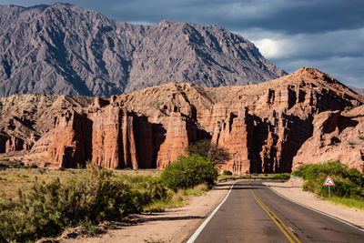 Road leading towards rocky mountains against sky