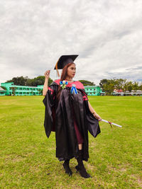 Portrait of woman wearing graduation gown standing on grassy field
