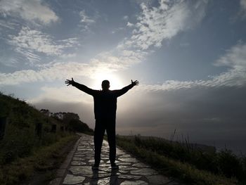 Rear view of man with arms outstretched standing against sky